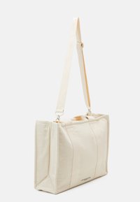 Kankainen viestintälaukku off-white-värissä, jossa on rakenteellinen muoto, kontrastiväriset ompeleet, kaksinkertainen kahva ja säädettävä hihna.