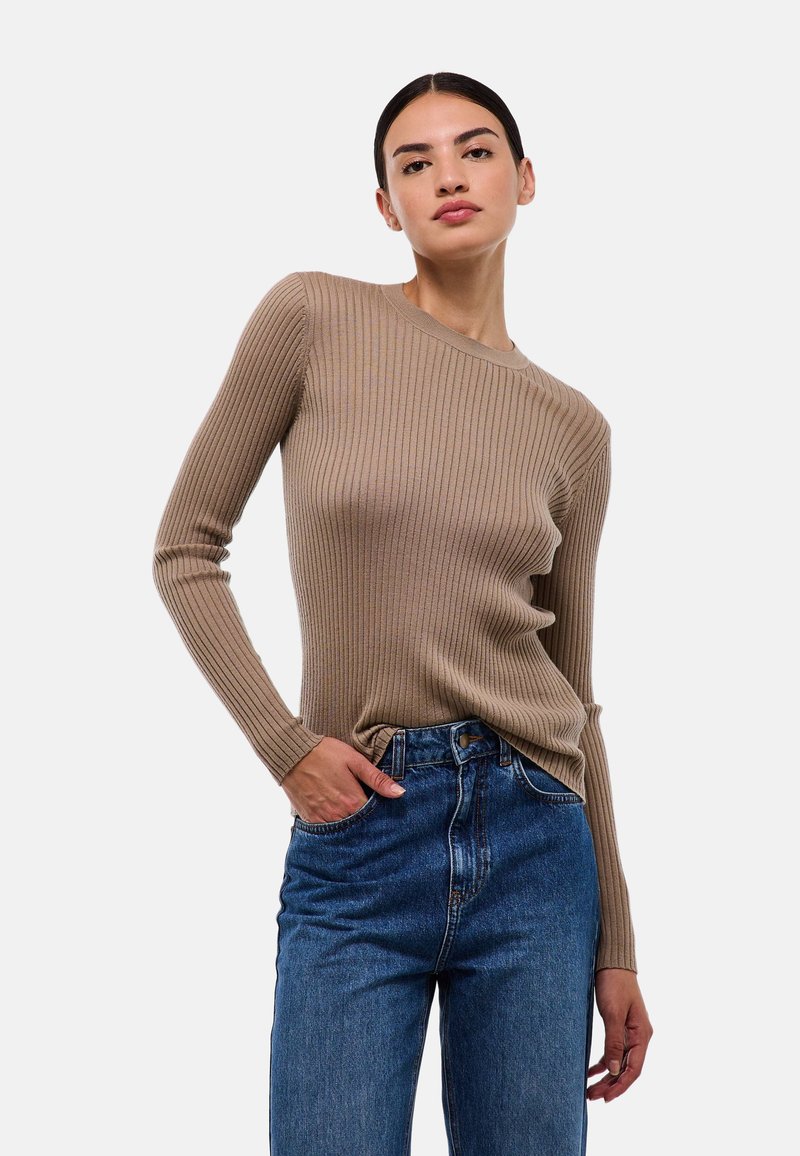 T-shirt beige à col rond à manches longues avec une coupe ajustée et une texture douce, assorti à un jean en denim bleu taille haute.