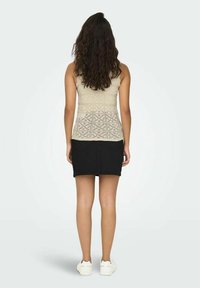 Beige crochet tank top with a fitted design, paired with a black denim skirt. The outfit is completed with white sneakers.