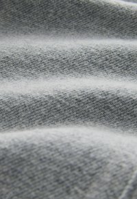 Šviesiai pilka tekstilė su subtiliu tekstūruotu raštu; raukšlės kuria gylį, parodantį minkštą, lygų paviršių.