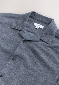 Donkerblauw shirt met korte mouwen, textuurstof, kraag en vier knopen aan de voorkant. Merketiket vermeldt "NEXT," maat MT.