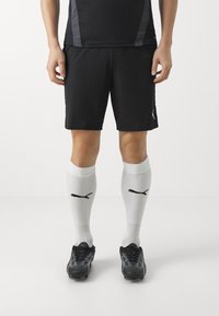 Svarta sportshorts, vita fotbollsstrumpor med svart logotyp och svarta fotbollsskor med texturerad design och en strömlinjeformad passform.