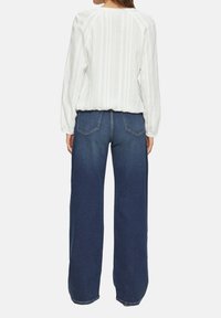 Witte top met lange mouwen en verticale strepen; gecombineerd met donkerblauwe wijde jeans met achterzakken en een lichte vervaging.