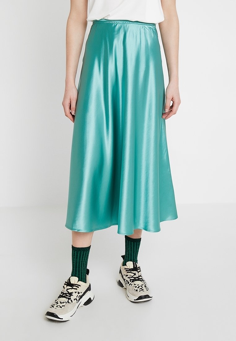 Tyrkysová saténová midi sukně s hladkou texturou, vybavená elastickým pasem a splývavou siluetou, stylizovaná s barevnými ponožkami a teniskami.