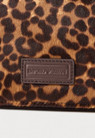 Motivo a stampa leopardata su un morbido materiale in pelliccia, con un'etichetta in pelle marrone impressa con "EMPORIO ARMANI" cucita lungo il bordo.
