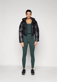 Melna saīsināta pūkaina jaka ar kapuci, kombinēta ar tumši zaļu piegulošu topu un legingiem. Raksturīga gluda dizaina un reljefa materiāla apvienojums. Melni sporta apavi.