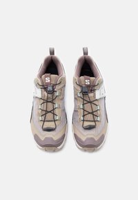 Ζευγάρι αθλητικά παπούτσια σε μπεζ και καφέ χρώμα με μαύρα ελαστικά κορδόνια και λευκές λουρίδες με βέλκρο, από πάνω σε λευκό φόντο.