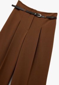 Bruine op maat gemaakte broek met voorplooien, een gladde stofstructuur en een zwarte leren riem met een zilveren gesp.