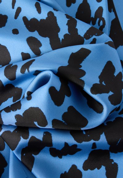 Tissu bleu soyeux avec des taches abstraites noires irrégulières, présenté en plis doux et en gros plan.