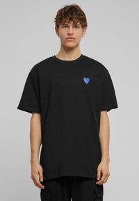 Sort bomulds t-shirt med rund hals og korte ærmer. Har et lille blåt hjerte grafik på venstre brystområde.