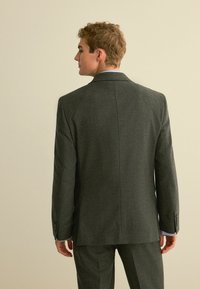 Grau karierter Blazer mit strukturierter Passform, ausgestattet mit einem einzelnen Schlitz und geknöpften Manschetten, kombiniert mit passenden Hosen und einem hellblauen Hemd.