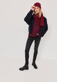 Cizme negre până la glezne, blugi negri skinny, top ribbed vișiniu, jachetă navy cu deschidere frontală și căciulă și eșarfă tricotate vișiniu corespunzătoare. Texturi netede.