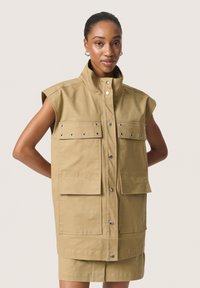 Khaki mouwloze utility vest met drukknoopsluitingen, voorzakken en metalen ogen; gemaakt van duurzaam materiaal met een gladde textuur.