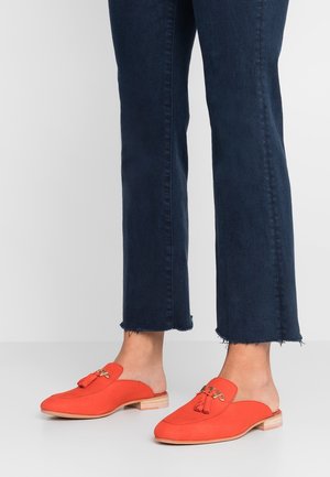 Oranje suède instapper mules met een kwastje, platte houten hak en een ronde neus. G gedragen met donkerblauwe jeans met een franjerand.