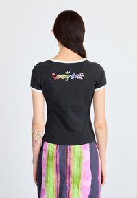 Sort tætsiddende t-shirt med korte ærmer og en hvid halsudskæring, med et flerfarvet "Jeremy Scott" tekstlogo på ryggen.