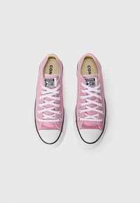 Pink canvas sneakers with white laces, black accents, and rubber toe cap. Features a logo tag on the tongue and a textured upper material.