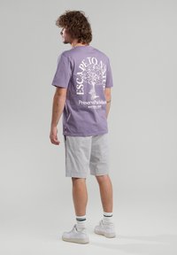 Lilac cotton t-shirt featuring a white graphic of a tree with text "Escape to Nature" and "Preserve Parkland" on the back, paired with gray shorts.