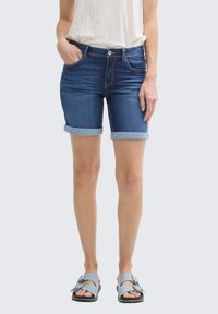 Shorts de mezclilla en azul oscuro con dobladillos enrollados, que cuentan con bolsillos frontales y un diseño ajustado, combinados con sandalias azul claro.