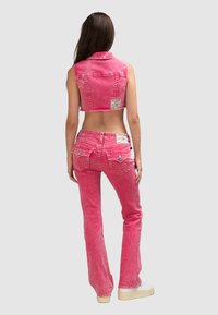 Różowa, krótsza kamizelka dżinsowa z kołnierzykiem, zestawiona z dopasowanymi spodniami. Posiada wyblakłą teksturę i dekoracyjne tylne kieszenie.