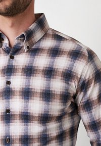 Geruit shirt in blauw, bruin en roomkleur. Bevat een button-down kraag, bruine knopen en een katoenachtige textuur.