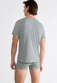 T-shirt aderente grigio chiaro con maniche corte e scollatura rotonda, realizzata in materiale morbido. Il design presenta una texture liscia e un branding minimale.