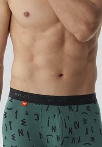 Zielone bokserki z czarną elastyczną talią z napisem "ATLANTIC." Wzór z czarnymi literami i symbolami w różnej wielkości.