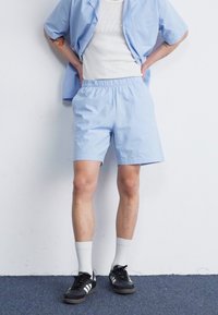 Cămașă scurtă cu mâneci scurte, de culoare albastru deschis, și pantaloni scurți asortați, confecționați dintr-un material neted. Pantalonii scurți au un tiv elastic și o croială lejeră.