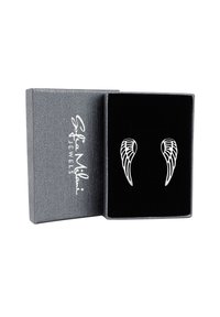 Silverfärgade vingeformade örhängen som visas i en svart sammetlåda med en skinande grå yta. Klara detaljer på vingarna.