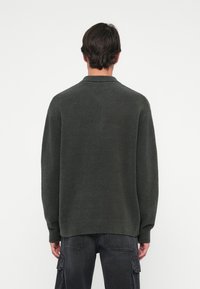 Maglione verde scuro, con texture, dal collo alto e vestibilità ampia. Polsini e orlo a costine, con schiena leggermente più lunga.