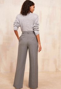 Grijze gebreide trui met opgerolde mouwen, gecombineerd met high-waisted, brede grijze broek met streepjes. Gladde textuur, op maat gemaakte pasvorm.