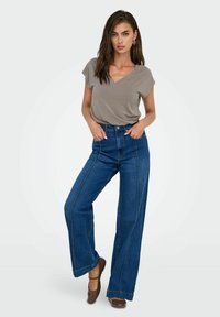 Camiseta gris de cuello en V combinada con jeans de mezclilla azul de tiro alto y pierna ancha. Los jeans tienen costuras de contraste y un ajuste relajado.