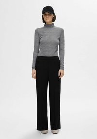 Grå langermet topp med høy hals, svarte vide bukser og en svart caps. Antrekket har en glatt tekstur og en nøytral fargepalett.