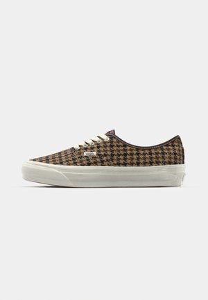Low-top sneaker made of brown houndstooth fabric with a white rubber sole, featuring beige laces and a small branded patch on the side.