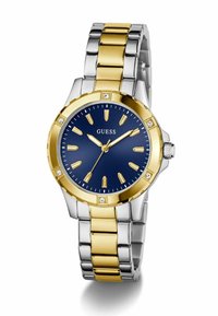 Montre en acier inoxydable argenté et doré avec un cadran bleu marine, des accents dorés et quatre petits gemstones sur la lunette. Les marqueurs d'heure sont allongés.