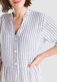 Vestido a rayas en lino azul claro y blanco, con escote en V, mangas cortas, cierre delantero de cuatro botones y cintura fruncida con bolsillos.