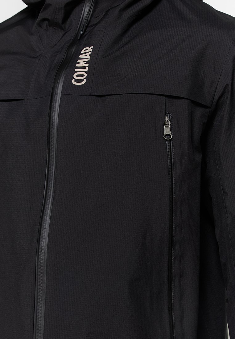 Giacca impermeabile nera con cappuccio, dotata di una zip frontale e di una tasca sul petto con zip. Tessuto texturizzato con dettagli riflettenti.