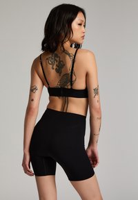 Reggiseno sportivo nero e pantaloni bike a vita alta, con una texture liscia e spalline regolabili. Corpo adornato con tatuaggi di inchiostro.
