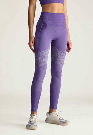 Lilla leggings med et struktureret mønster i en lysere nuance, høj talje og kontrastsyninger, parret med neutrale atletiske sko.