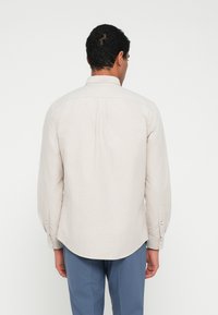 Svetlobéžová košeľa s dlhým rukávom z textúrovaného materiálu. Má zadnú časť s dielom, zaoblený spodný lem a manžety na gombíky.