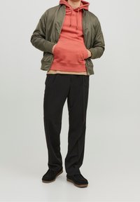 Cazadora bomber de color oliva, sudadera con capucha coral, camisa beige, pantalones negros y zapatos negros sin cordones. Tejidos suaves, look casual en capas.