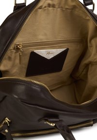 Wnętrze torby z ciemno brązowej skóry z złotym zamkiem błyskawicznym. Zawiera kieszeń zamykaną na zamek oraz kieszonkę na kartę. Podszewka w jasnym beżowym kolorze.