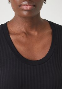 Černý žebrovaný top s kulatým výstřihem, texturovanou látkou a slim fit střihem. Mezi detaily patří hladké okraje a jemný lesk.