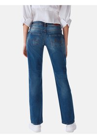 Vaqueros de denim azul con corte recto, que cuentan con bolsillos traseros cosidos y un ligero desgaste. Llevados con zapatillas blancas.