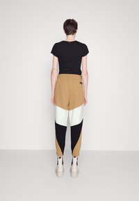 Black T-shirt, brown, white, and black color-blocked joggers with elastic waistband and cuffs, complemented by chunky beige boots.