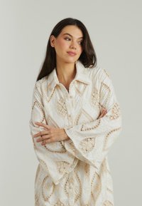 Blusa color avorio con pizzo, maniche a campana; presenta intricati disegni cuciti e un colletto con chiusura a bottoni.
