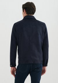 Marinblå faux läderjacka med en slät yta, skräddarsydd passform och synliga stygn. Har en vikbar krage och tryckknappsmuddar.