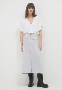 Top bianco corto con scollatura a V, abbinato a una lunga gonna grigia chiara con zip laterale e tasca frontale, completato da stivali neri.