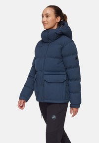 Fodrad jacka i mörkblått, med hög krage, tryckknappar, två framfickor och logotypemblem på ärmen. Strukturerad, isolerad design.