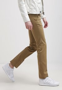 Beige, smala byxor i mjukt tyg med en slät yta och framfickor. Matcher med vita sneakers för kontrast.