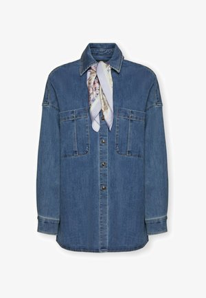 Camicia di jeans con due grandi tasche sul petto e una sciarpa di seta a motivo annodata intorno al colletto su sfondo bianco.